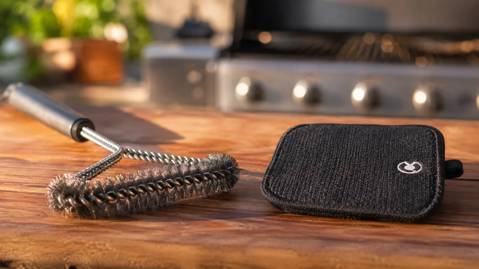 Two bristle-free grill brushes resting on the edge of a charcoal grill grate, ember-lit backyard background at dusk