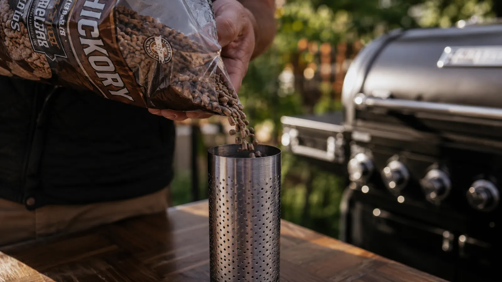 LIZZQ pellet smoker tube lying on a cutting board surrounded by small piles of different wood pellets in hickory, apple, and cherry