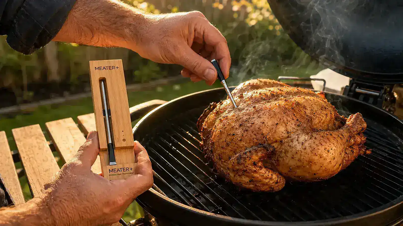MEATER Plus charging dock standing on an outdoor side table next to a grill, probe resting inside the bamboo block charger