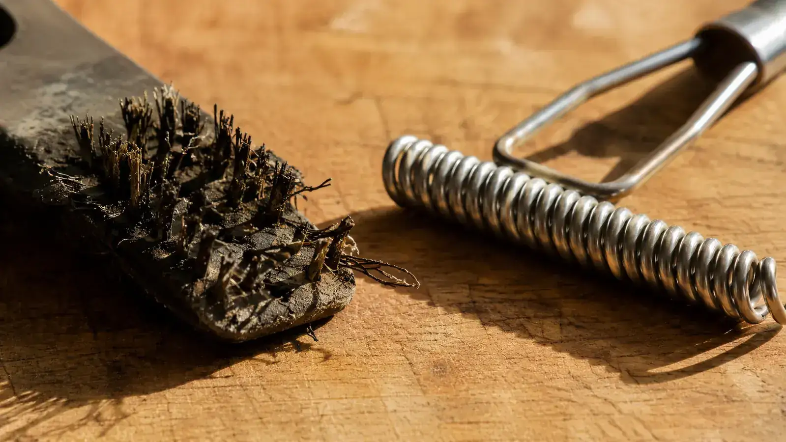 Close-up of a wire grill brush with a loose bristle compared to the coiled stainless steel head of the Kona brush